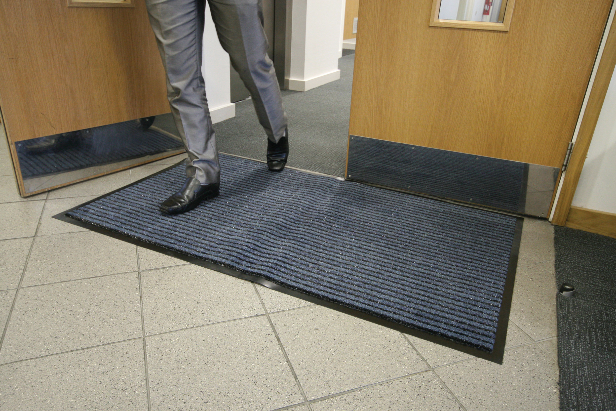 Man walking through doors ontop of a Blue/Black Double Action Doormat