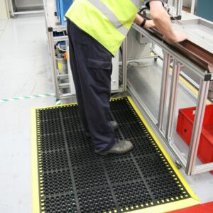 Man stood at a workstation on a black/yellow deluxe workplace mat