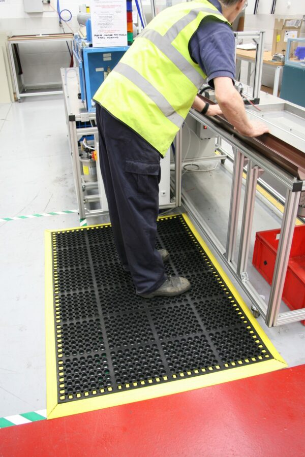 Man stood at a workstation on a black/yellow deluxe workplace mat