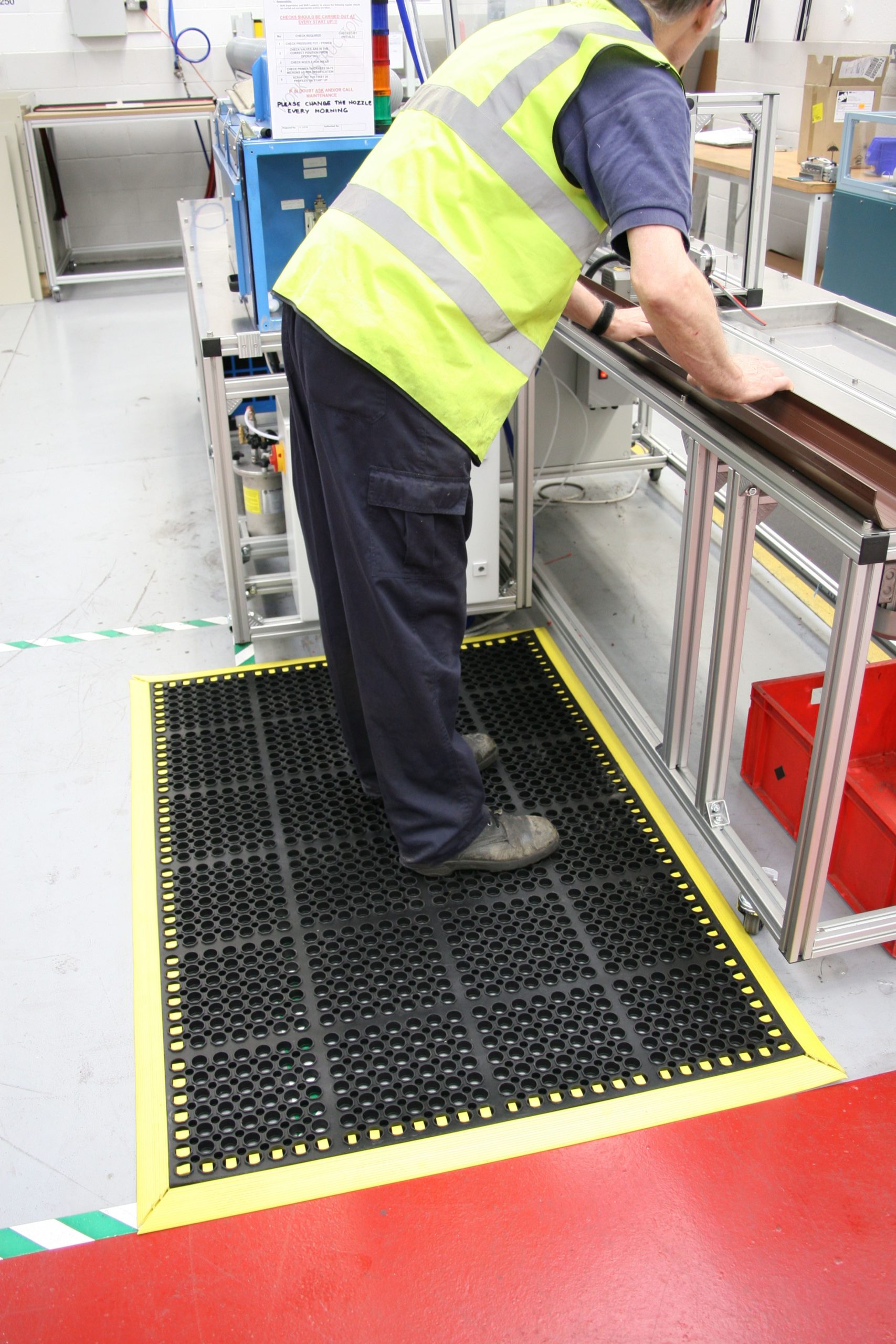 Man stood at a workstation on a black/yellow deluxe workplace mat